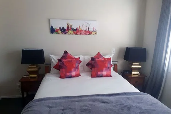 Bedroom with white bedding, red decorative pillows, and a city skyline print above the headboard.
