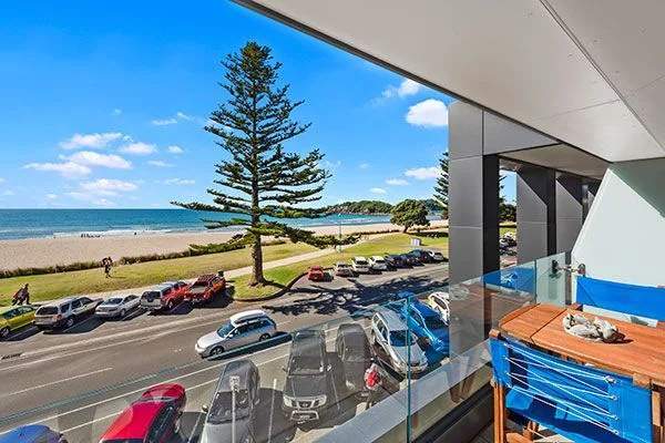 Balcony view of beachfront street, parked cars, and ocean at Mount Maunganui.