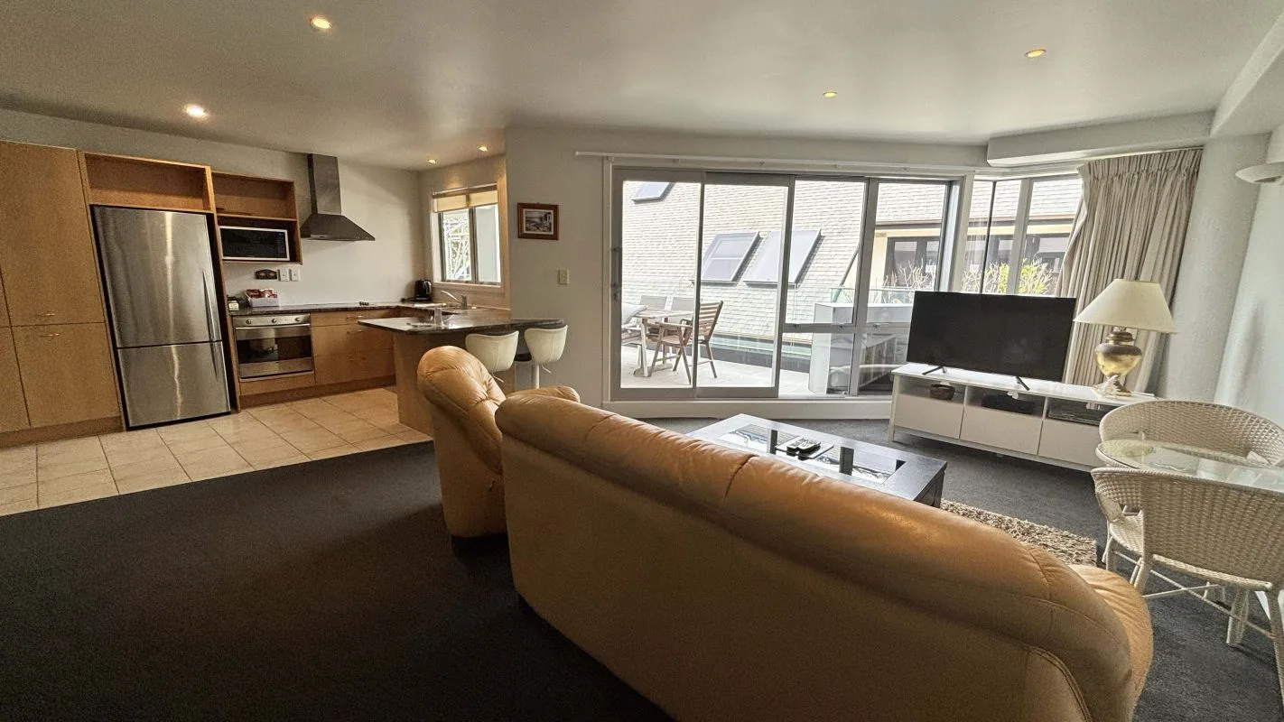 Open-plan living room and kitchen with leather sofas and balcony access.