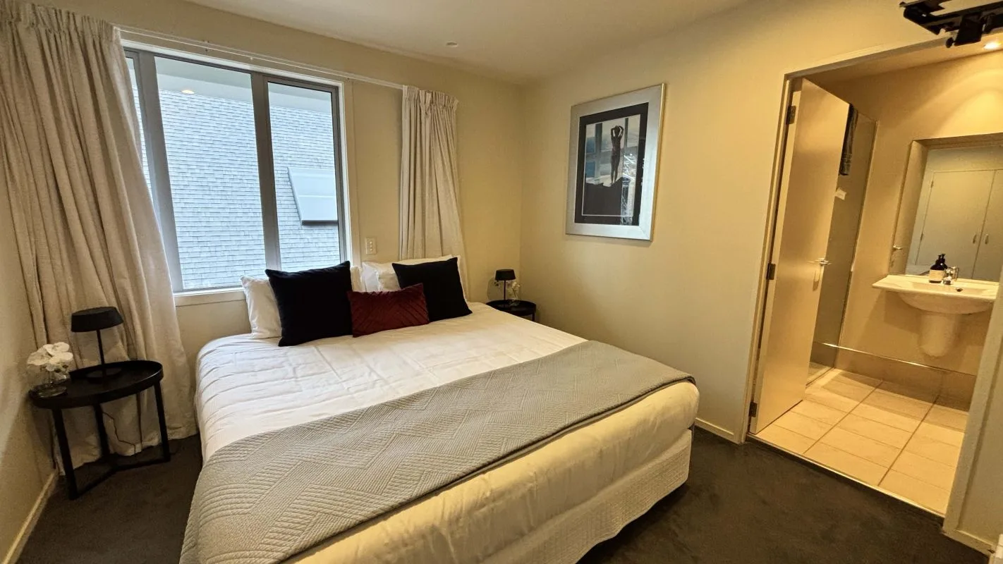 Bedroom with white bedding, black accent pillows, and adjoining bathroom with sink.