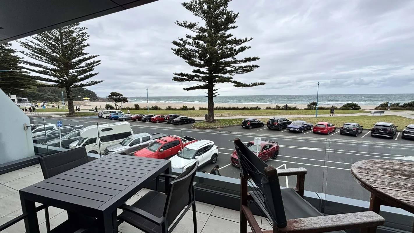 Balcony view of parked cars, pine trees, and beach with ocean.