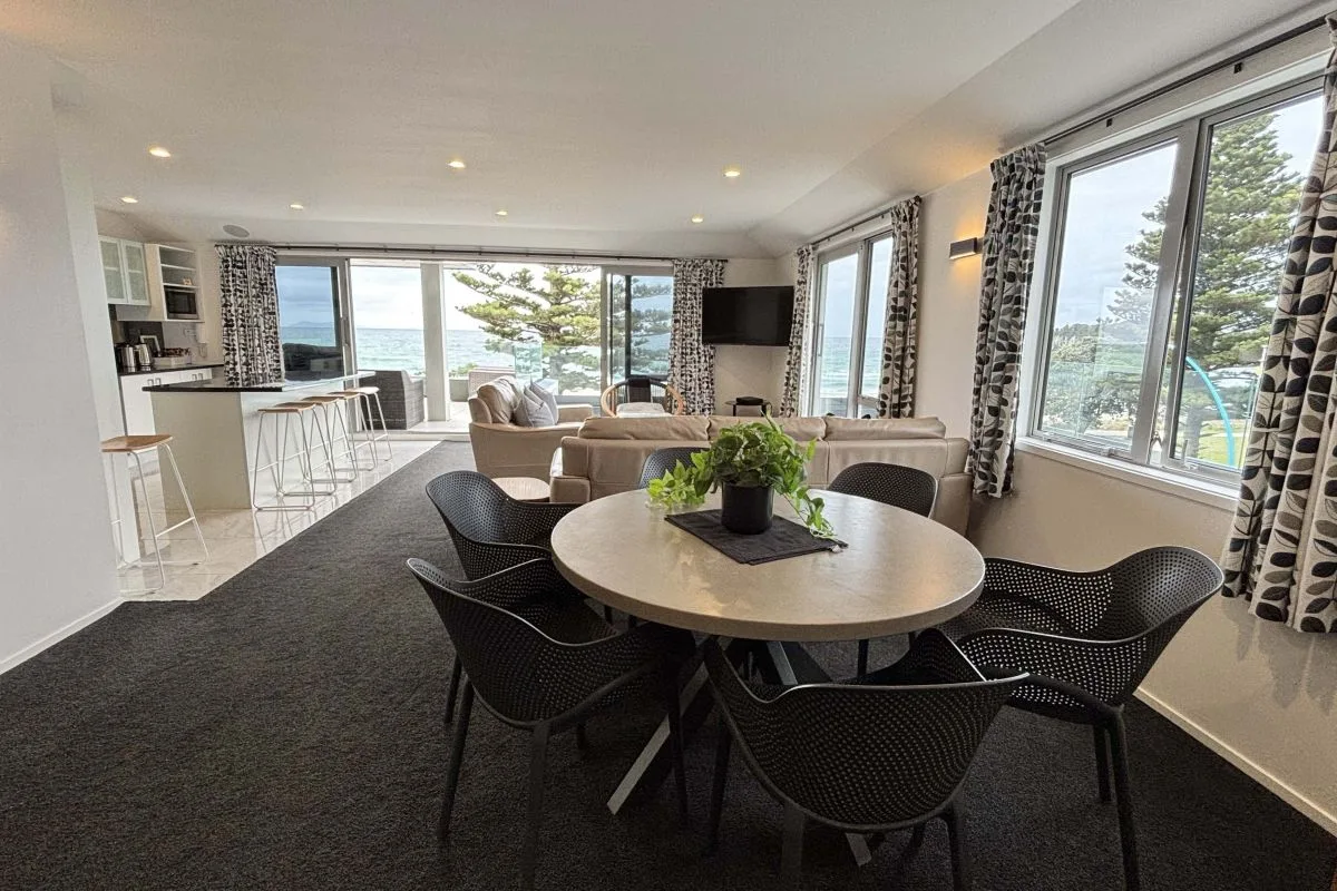 Open-plan living area with dining table, bar stools, and ocean-view windows.