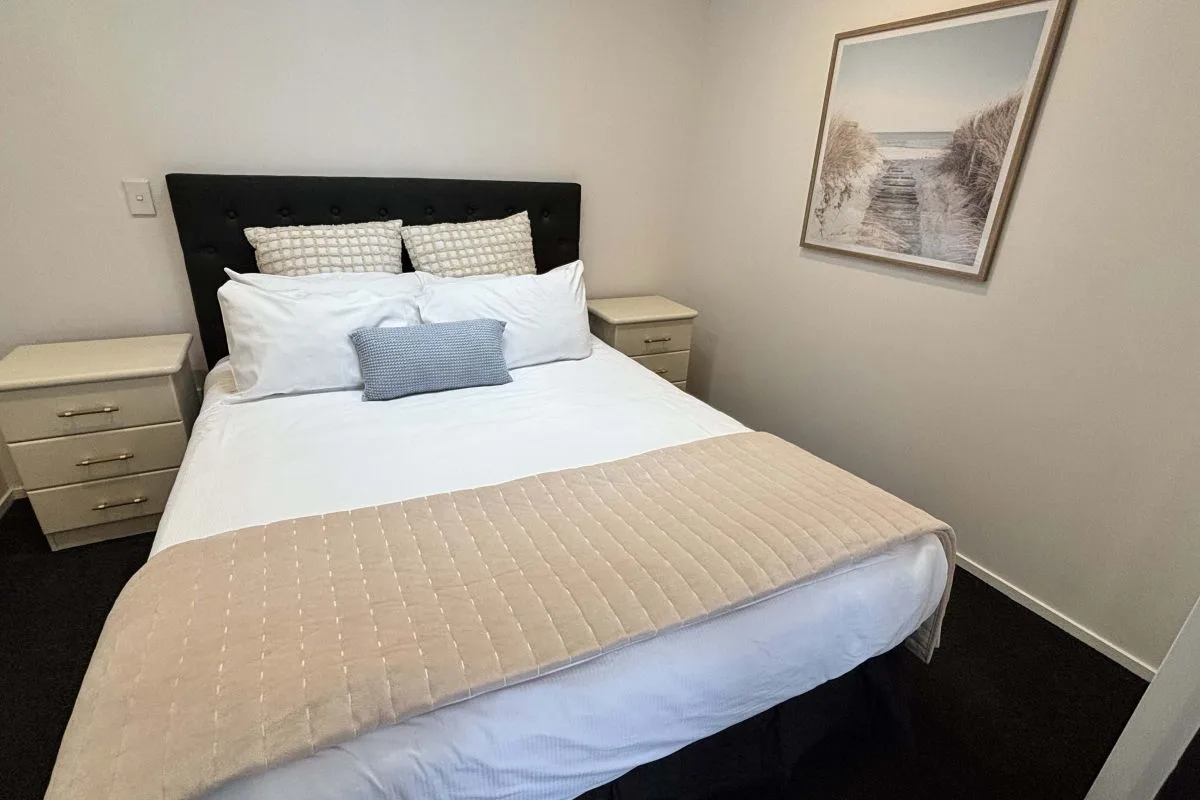 Bedroom with upholstered headboard, layered pillows, and beach-themed wall art.