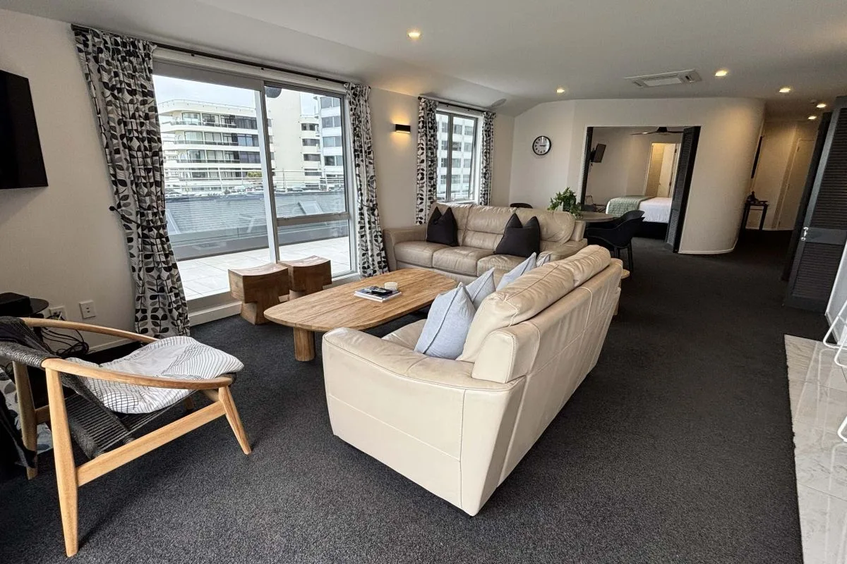 Living room with cream leather sofas, wooden coffee table, and city view balcony.