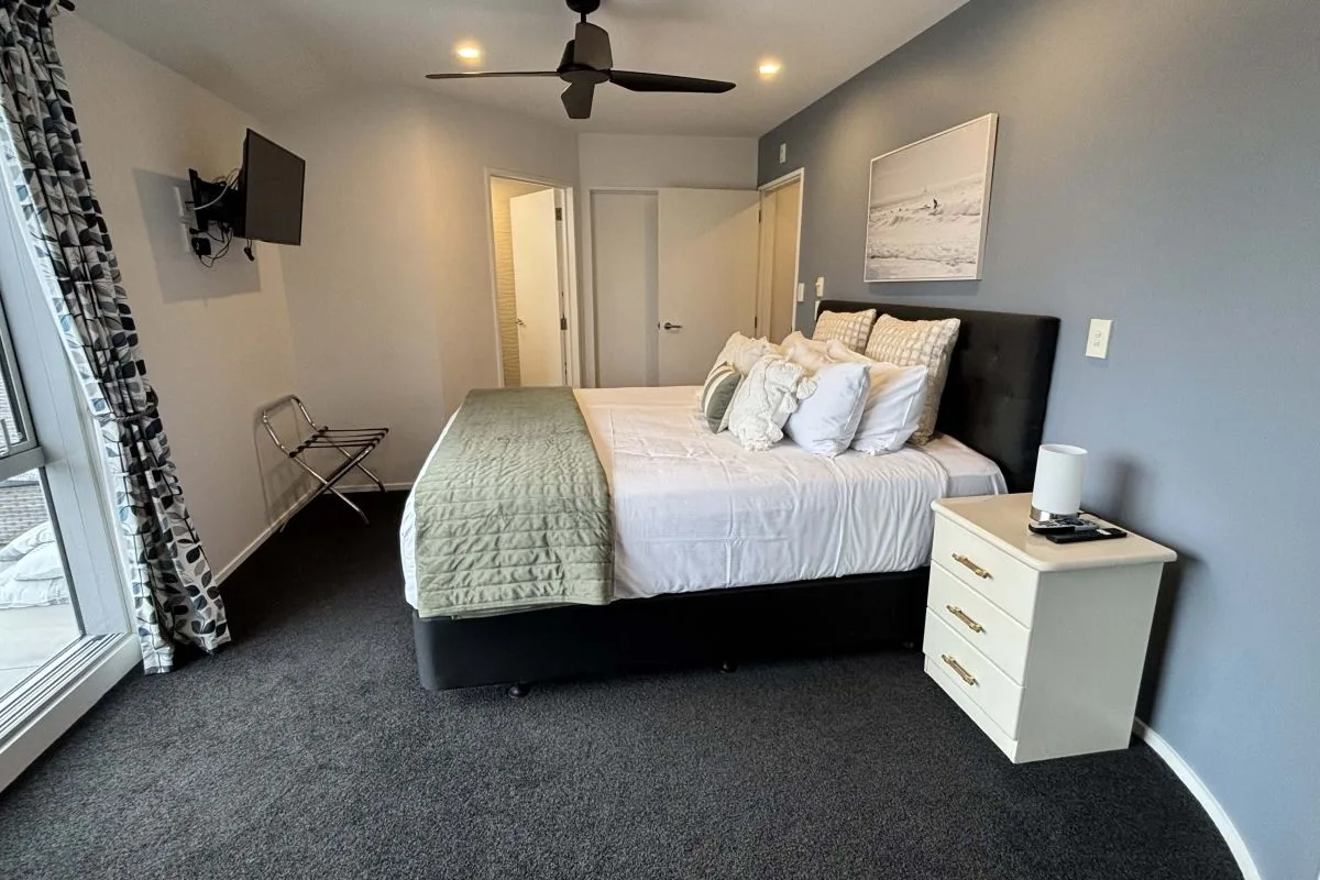 Bedroom with black-framed bed, white nightstand, wall-mounted TV, and ceiling fan.