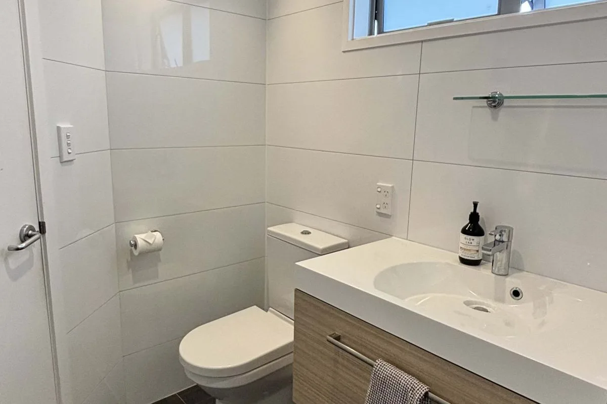 Bathroom with wall-mounted toilet, tiled walls, and vanity sink unit.