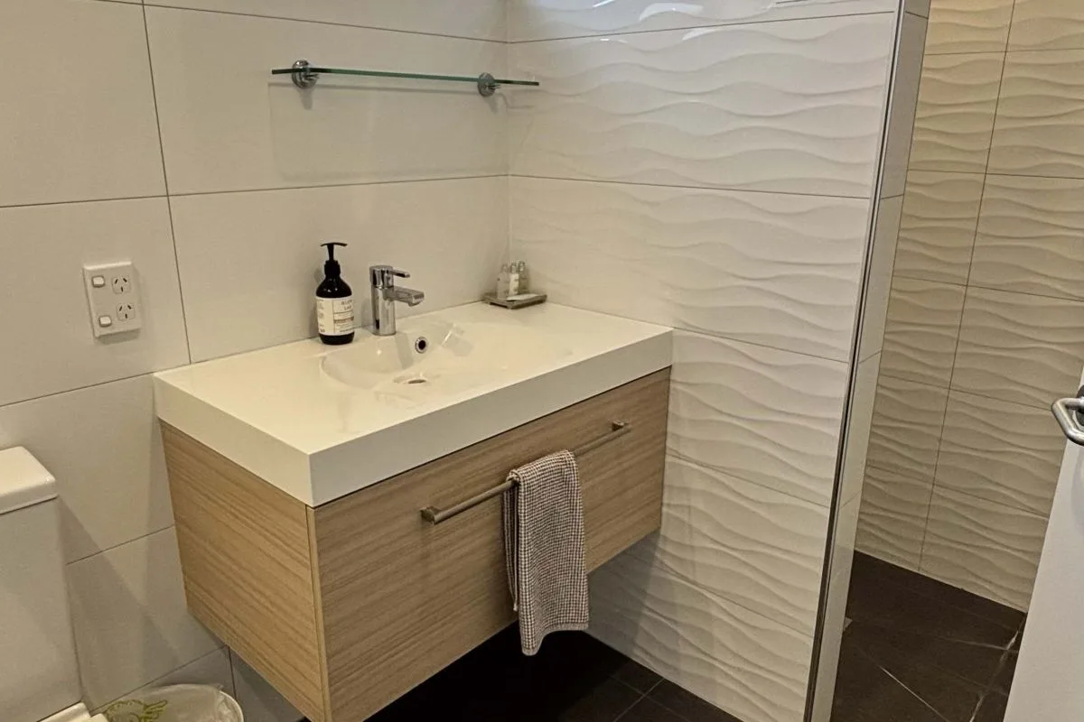 Bathroom vanity with wall-mounted sink, wooden cabinet, and glass shower enclosure.