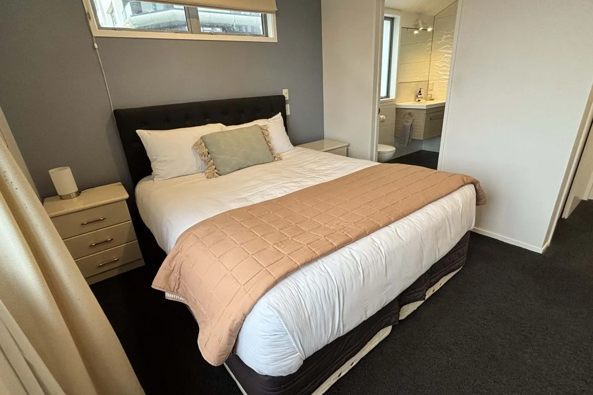 Bedroom with black tufted headboard, white bedding, and peach quilted throw.